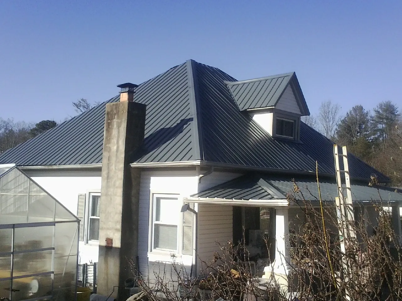 Dark blue standing seam metal roof on a white farmhouse with dormer — Slate & Tile Roof Repair by Roofing Brothers in Stone Mountain