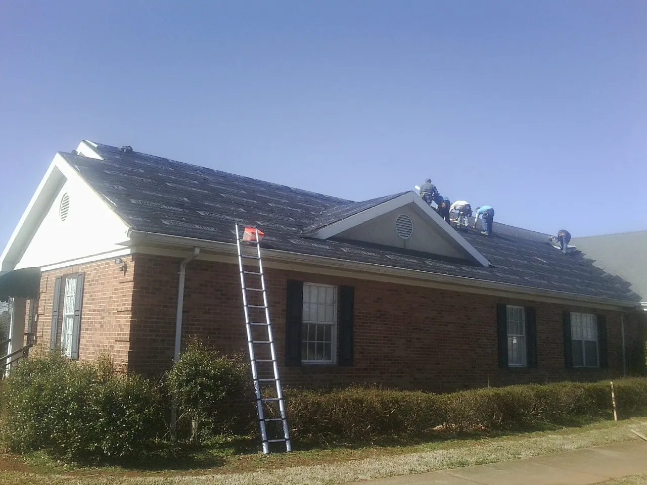Crew tearing shingles off a brick ranch roof with a ladder set — Emergency Roof Repair work by our crew in Stone Mountain