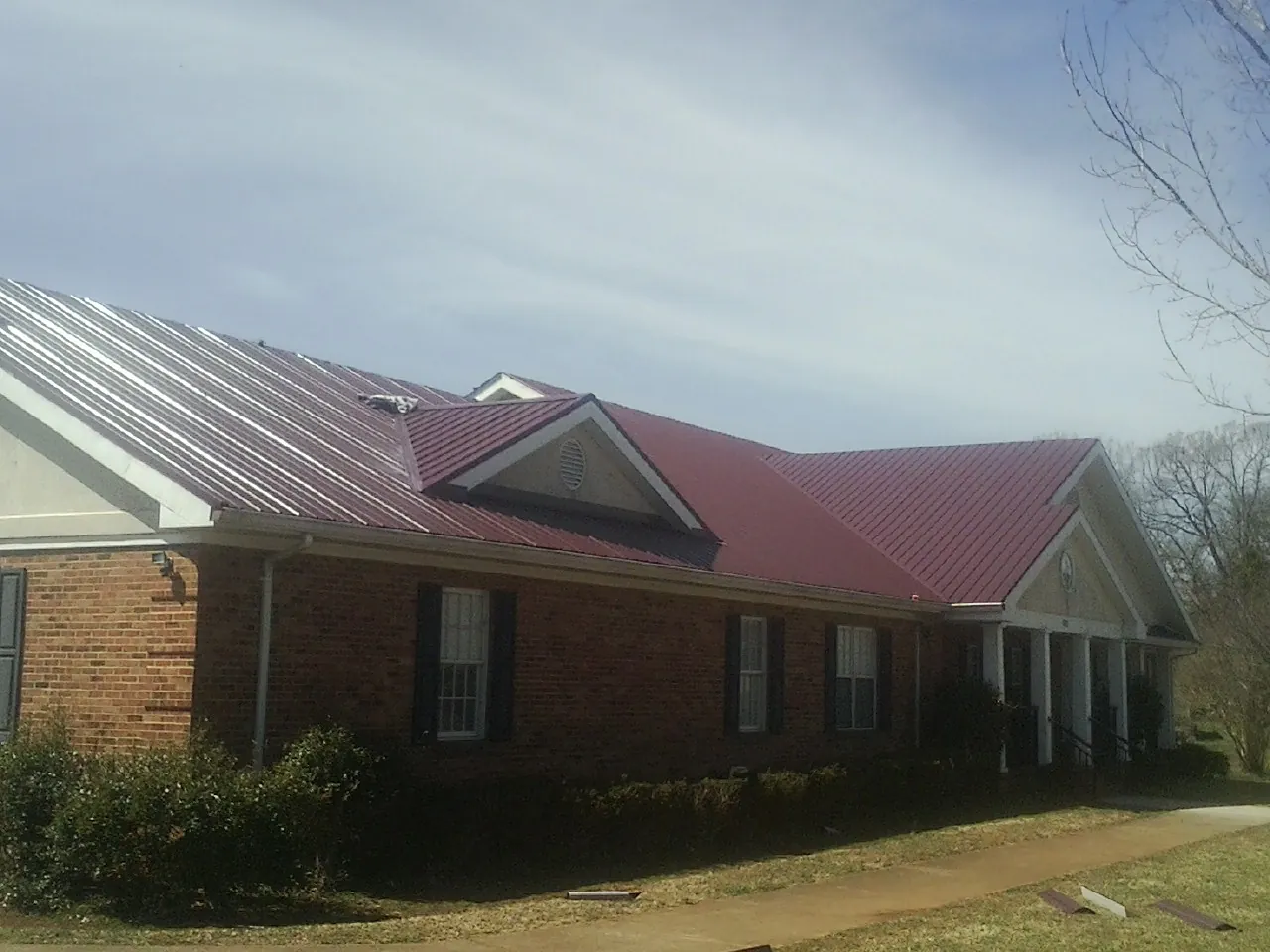 Red metal roof with gabled entries on a long brick building, from a Hail Damage Roof Repair job in Stone Mountain