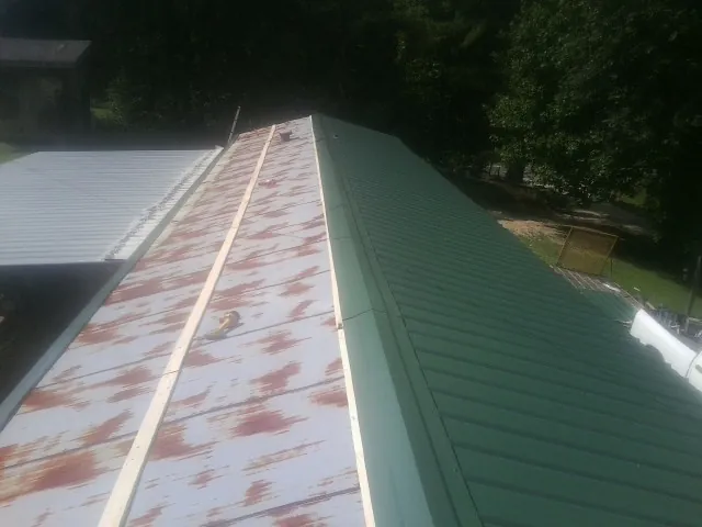 Old rusted panels beside newly installed green metal roofing — Wind Damage Roof Repair by Roofing Brothers in Stone Mountain