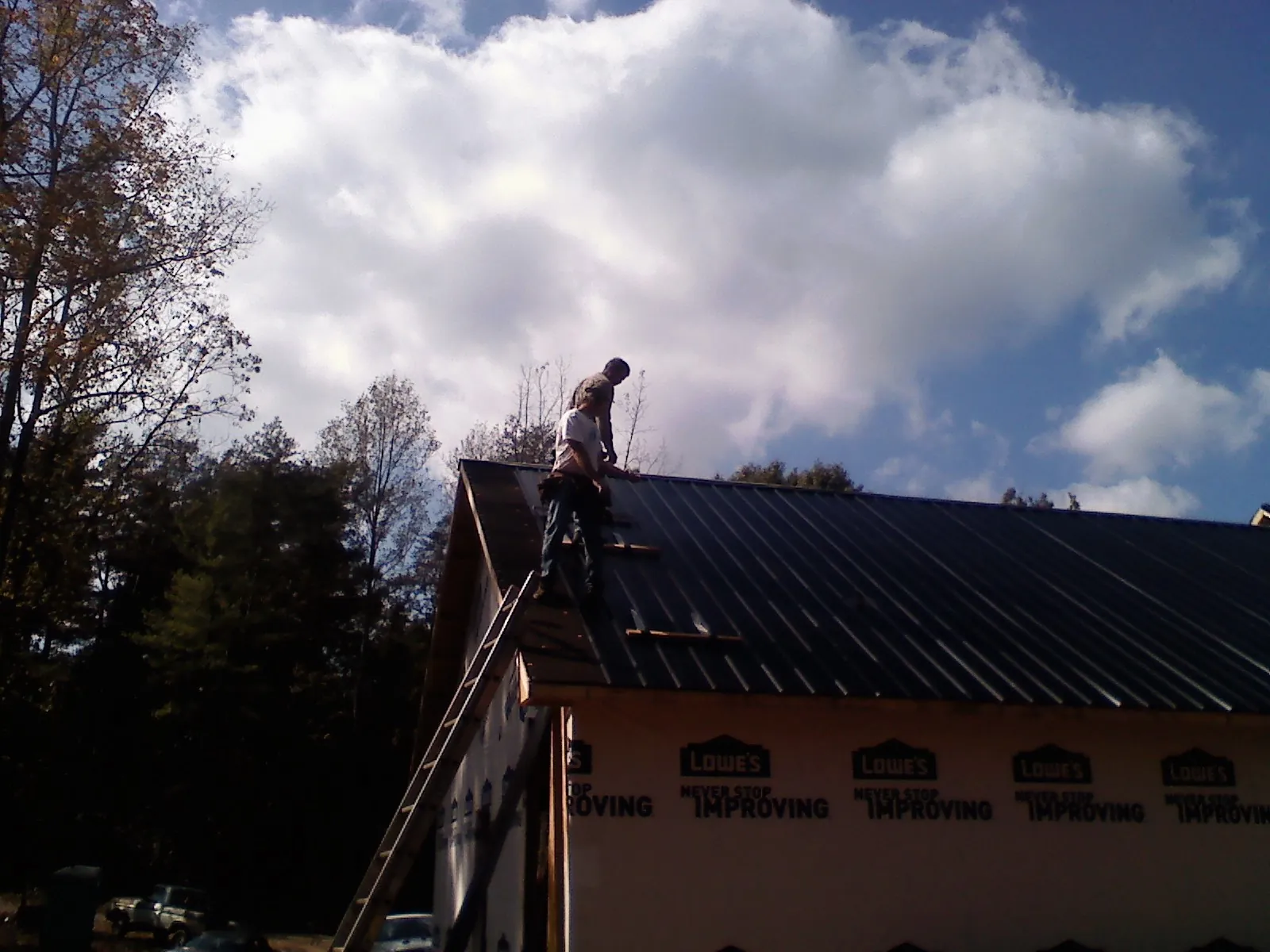 Roofer fastening dark metal panels high against a cloudy sky, from a Roof Inspection job in Stone Mountain