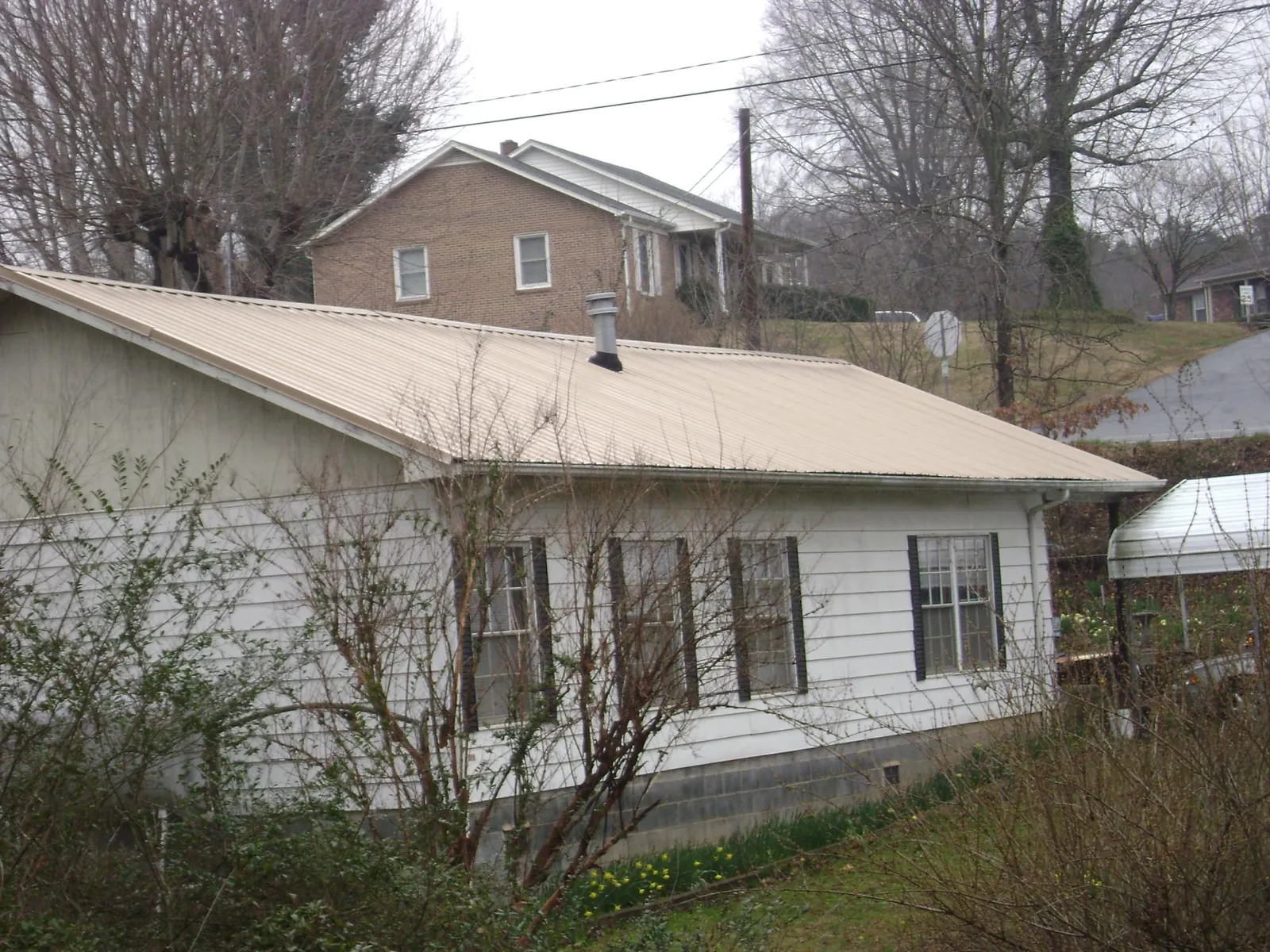 Tan metal roof on a white sided house set into a hillside — Commercial Roofing by Roofing Brothers in Stone Mountain
